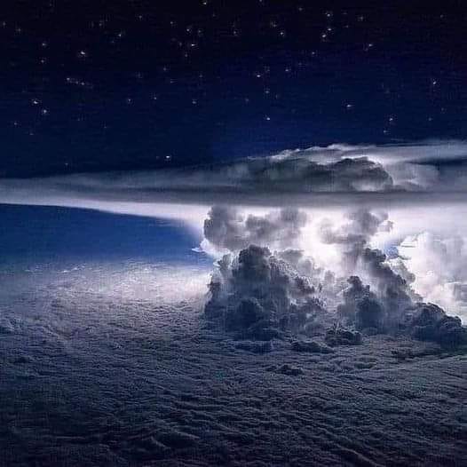 Illuminated storm clouds rising above a cloud layer at night beneath a starry sky