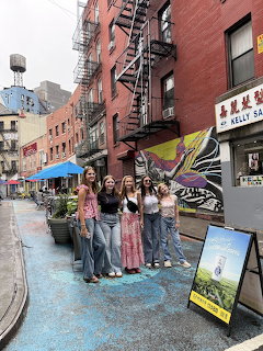 Group of five young women posing on a colorful Chinatown street in New York City with murals and fire escapes