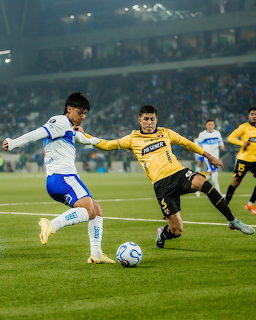 Soccer player in white jersey dribbling ball while defender in yellow attempts to block during night match