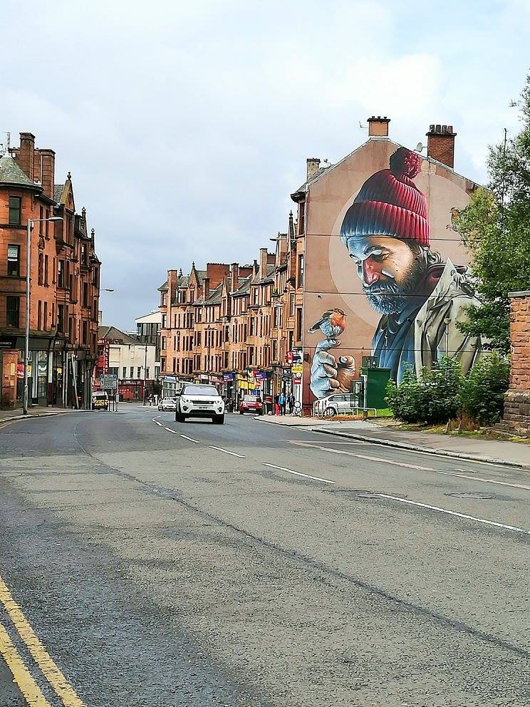 Glasgow street with brick buildings and a large mural of a bearded man on a corner building