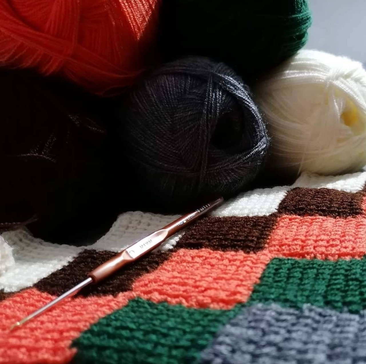 Colorful yarn balls with a crochet hook resting on a crocheted blanket