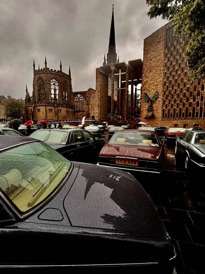 Vintage cars parked beside the ruins of Coventry Cathedral on a cloudy day