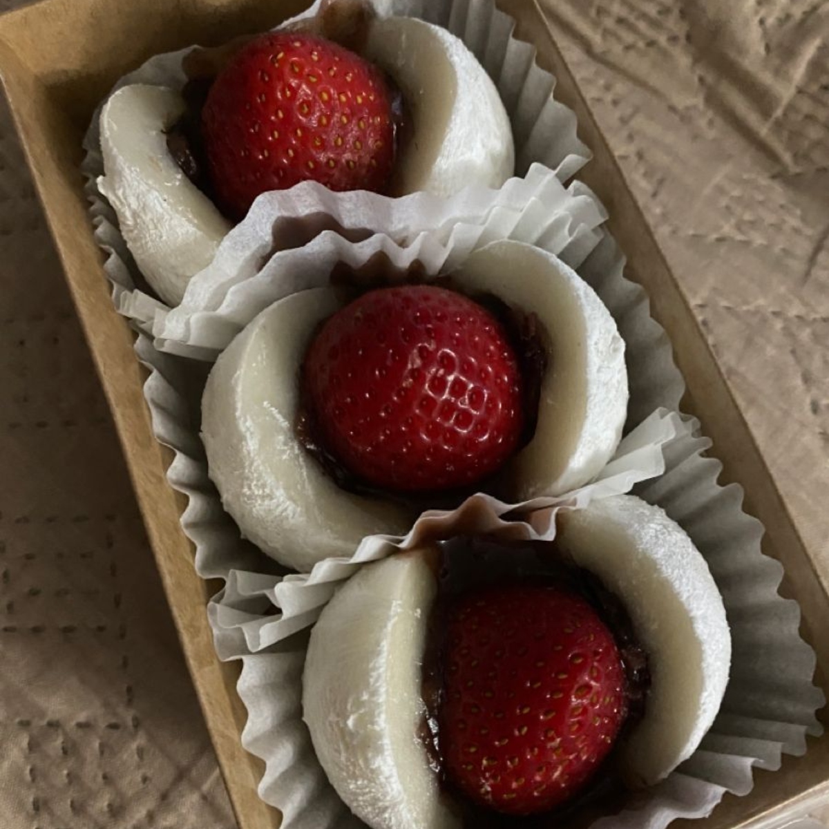 Three strawberry daifuku mochi with red strawberries in white paper cups
