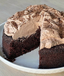 Dark chocolate cake with chocolate frosting and cocoa powder on a white plate with one slice missing