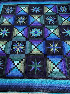 Geometric quilt with star patterns in blue, purple and turquoise on black fabric
