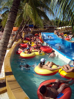 People on colorful inflatable tubes floating in a lazy river at a tropical water park with palm trees