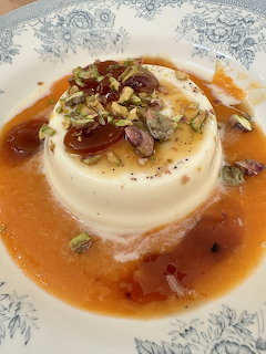 White panna cotta dessert with caramel sauce and nut topping on ornate plate