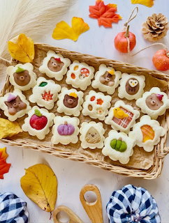Wicker basket of kawaii decorated cookies with autumn themes surrounded by fall leaves and miniature pumpkins