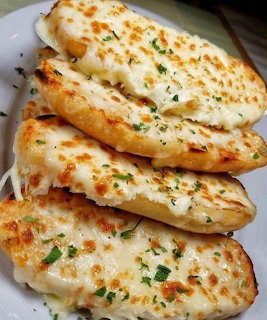 Stack of golden toasted garlic bread slices with melted cheese and herbs on white plate