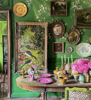 Vibrant green dining room with gallery wall, tropical art, ornate table set with colorful dishes and pink flowers