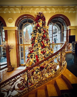 Decorated Christmas tree on ornate staircase in Victorian mansion with arched windows and polished wood floors