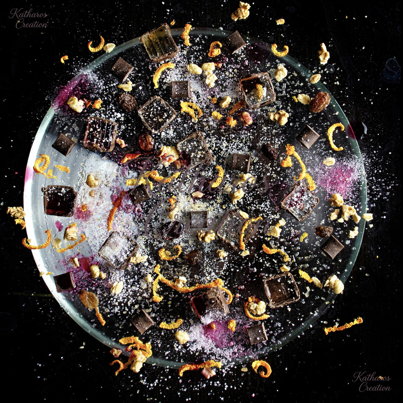 Overhead view of a round platter with chocolate desserts, powdered sugar, and scattered colorful crumbs
