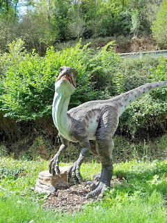Dinosaur statue in a grassy garden with green bushes behind it