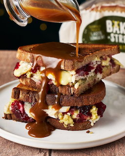 Triple-stacked sandwich with gravy being poured over it, filled with eggs, bacon and cheese on toasted bread