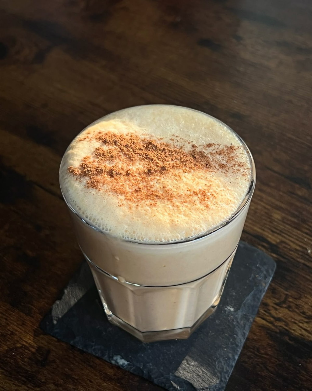 Latte with cinnamon dusting in glass on slate coaster
