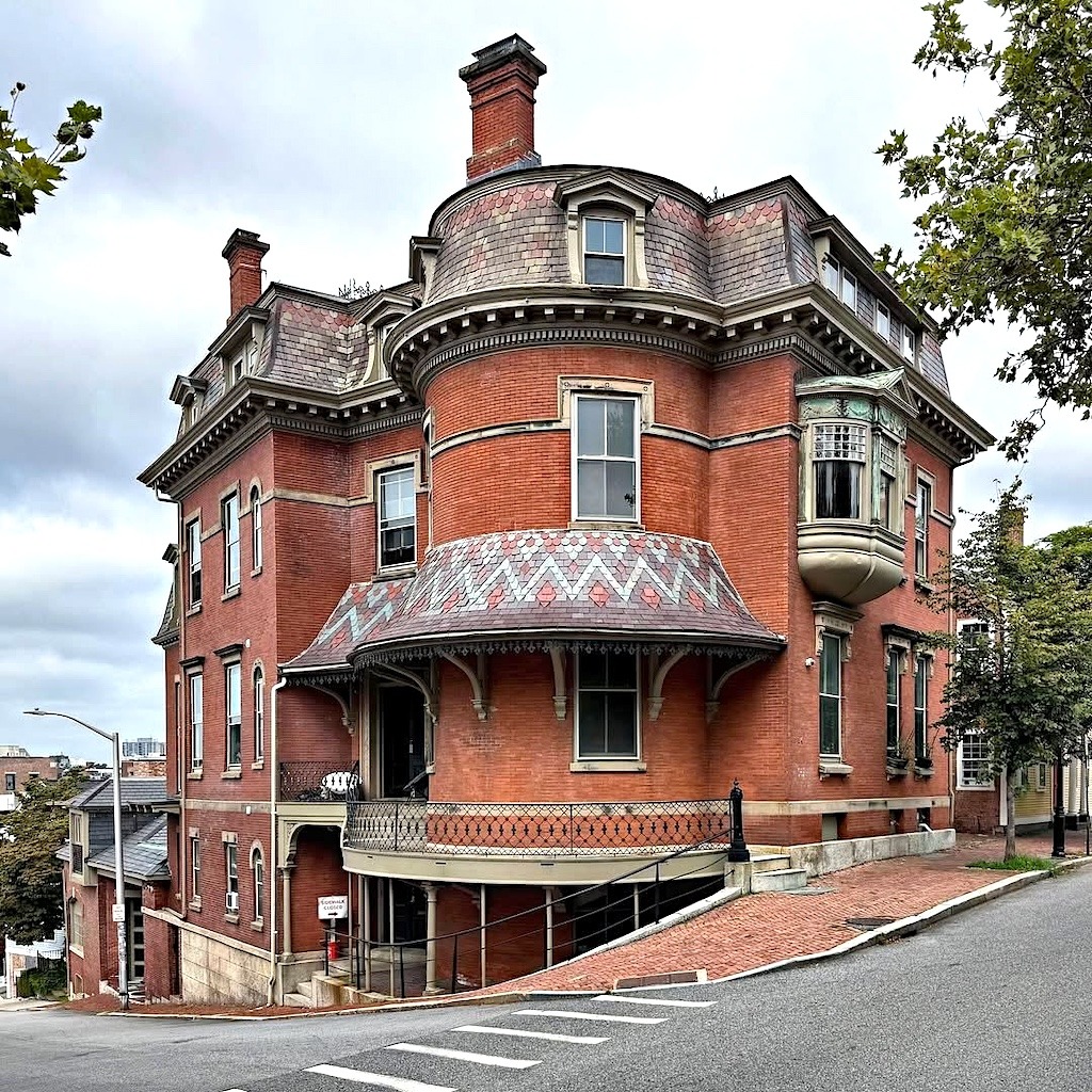 Historic red brick Victorian house on a steep street corner with ornate roof trim and bay windows