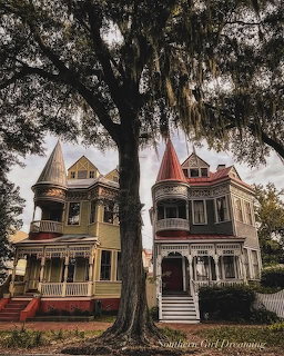 Two Victorian houses with turrets and pointed roofs under a large oak tree with Spanish moss