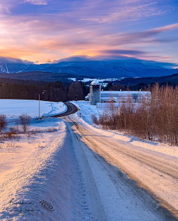 Snowy country road at sunset with mountains and farmland in Vermont winter landscape