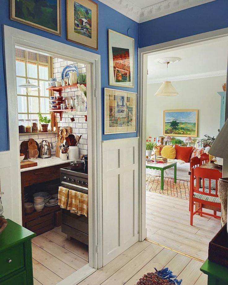 Eclectic home interior with blue walls, framed art, open doorways showing kitchen nook and colorful dining room