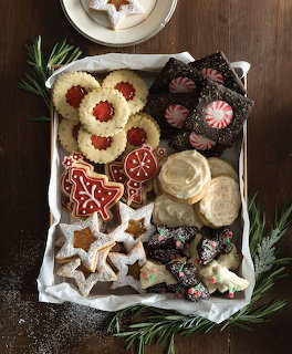 Assorted Christmas cookies in white box with holiday decorations and evergreen sprigs on wooden surface