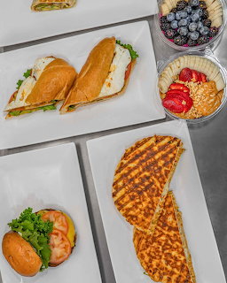 Overhead view of breakfast dishes including croissant sandwiches, waffle, burger, and yogurt bowls on white trays