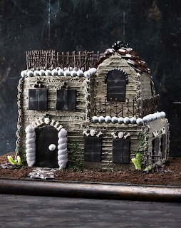 Multi-tiered haunted house cake with intricate gray frosting, black windows, and Halloween themed decorations