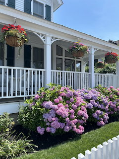 White house front porch with blooming pink and purple hydrangeas and hanging flower baskets