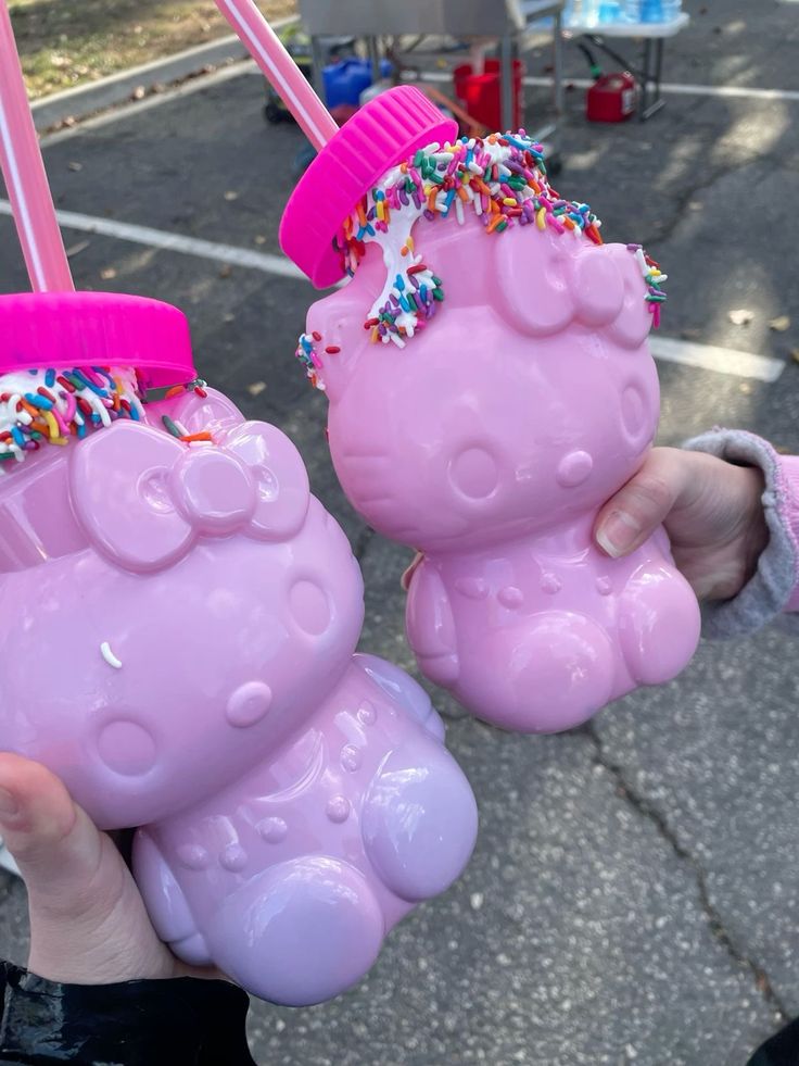 Two pink Hello Kitty milkshake cups with straws and rainbow sprinkles being held outside