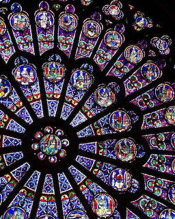 Circular stained glass rose window with colorful biblical panels radiating from center in Gothic cathedral style
