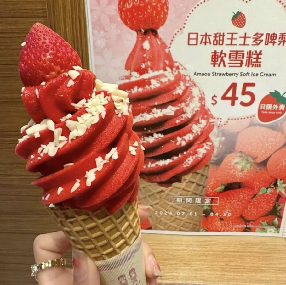 Red strawberry soft serve ice cream cone with white chocolate drizzle and strawberry topping