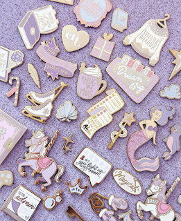 Pastel enamel pins on a purple background with shoes, shells, a horse, and other whimsical designs.