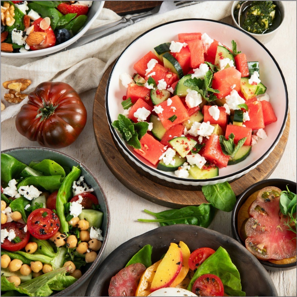 Colorful fresh salads in bowls with watermelon, strawberries, greens, chickpeas, and feta cheese