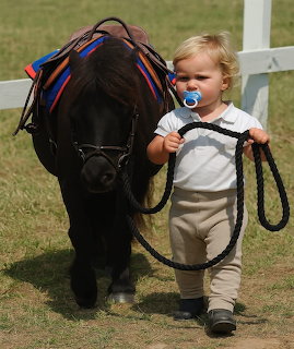 Toddler walking beside a black pony while holding its lead rope outdoors