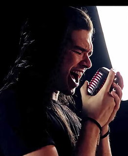 Long-haired metal musician in dark clothing posing for a portrait