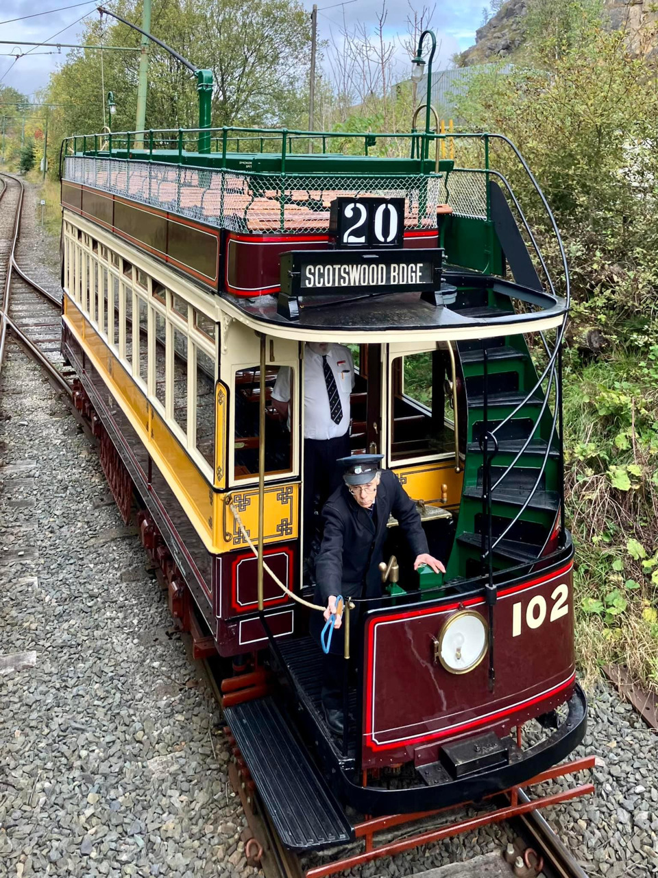 Vintage double-decker tram 102 in burgundy and yellow on tree-lined track