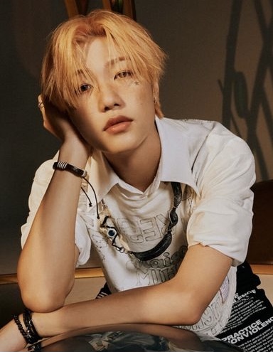 Young man with blonde hair wearing white shirt, hand near face, looking at camera