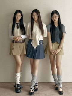 Three young women in coordinated skirts and tops posing against a plain wall indoors
