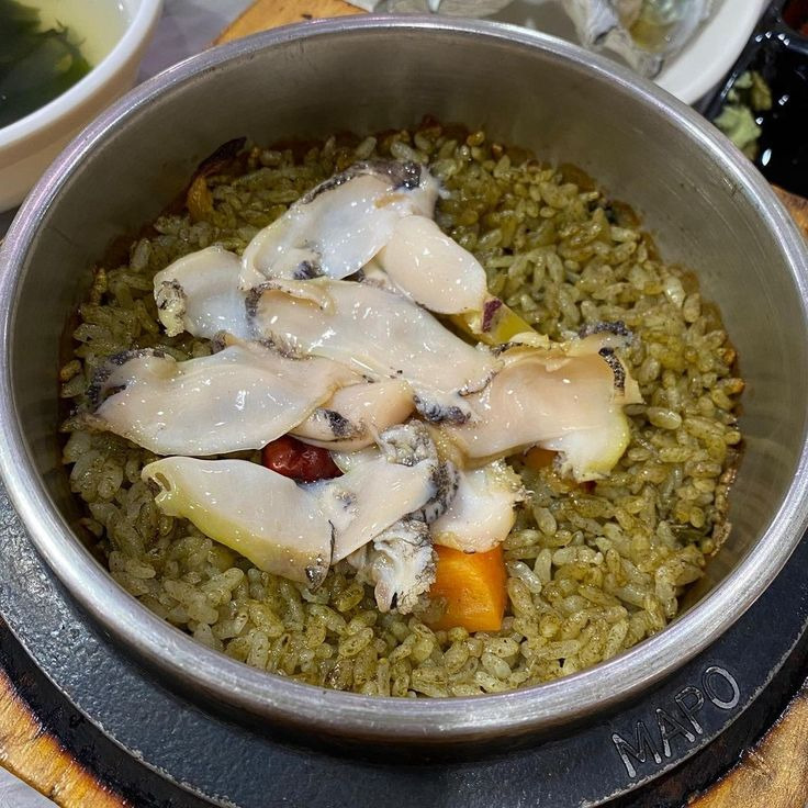 Bowl of abalone porridge with sliced seafood and rice in metal pot