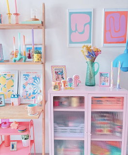 Colorful pastel interior with pink cabinet, wooden shelf, candles, art prints, and bright decorative items
