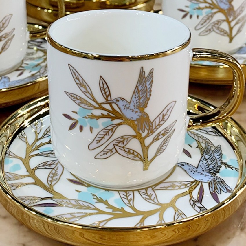 White porcelain teacup with gold trim and floral bird design on matching saucer