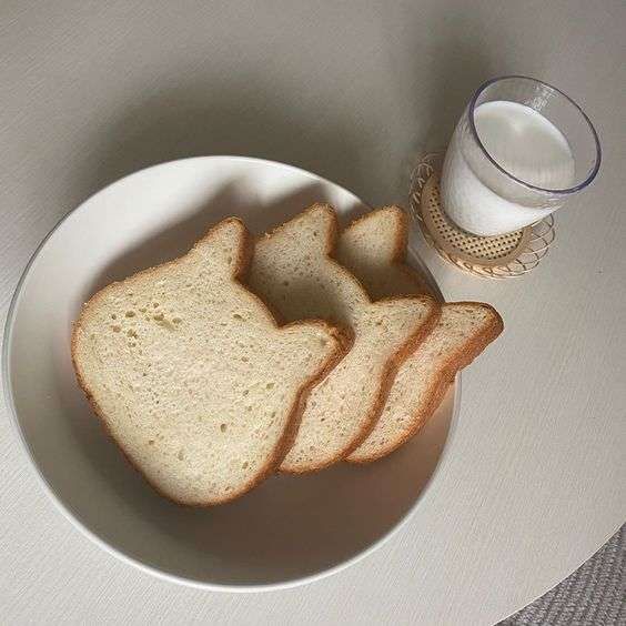 Cat-shaped bread slices on white plate beside glass of milk