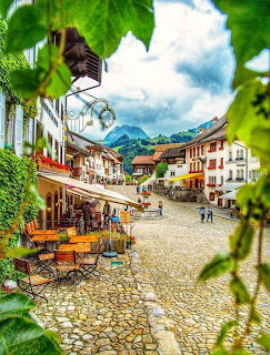 Cobblestone square in Alpine village with traditional buildings, cafes, mountains, framed by ivy leaves