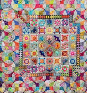 Colorful patchwork quilt with geometric kaleidoscope patterns and floral blocks surrounded by pieced triangle borders
