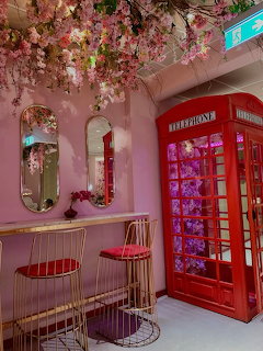 Pink café interior with cherry blossoms, gold chairs, mirrors, and a red telephone booth