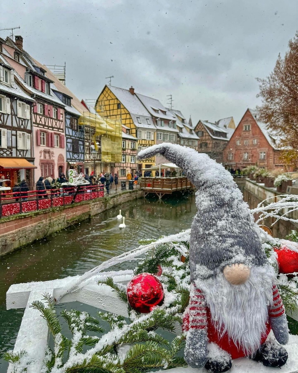 Christmas gnome decoration overlooking a snowy canal in Colmar with colorful traditional buildings