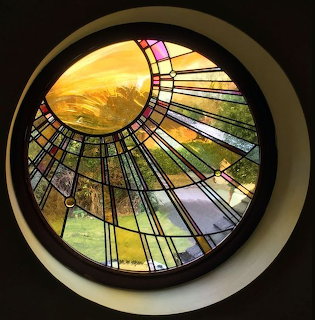 Circular stained glass window with geometric panes and a sunlit landscape beyond