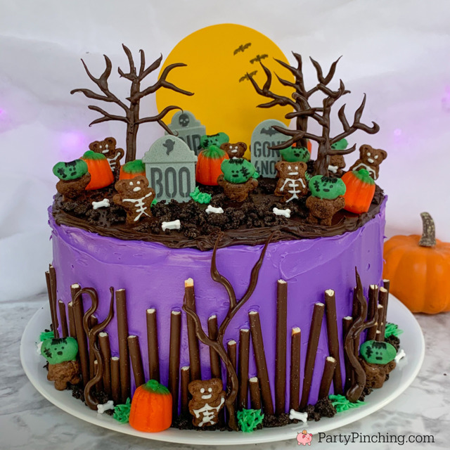 Purple Halloween cake with tombstones, pumpkins, skeletons, and bare trees on top