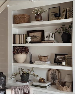 White built-in bookshelf with books, vases, baskets, framed art, and dried flowers in neutral earth tones