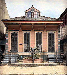 Pink shotgun house with star decoration in gable and wrought iron fence