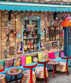 Colorful cafe exterior with patterned chairs, painted tables, and eclectic decorations on a stone building